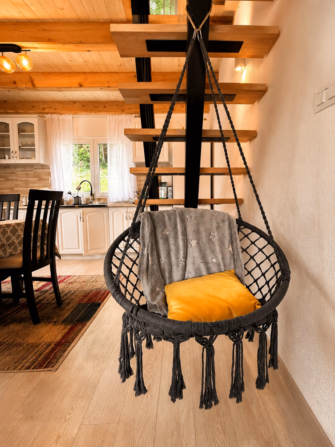Hanging swing chair inside the cabin with kitchen and wooden stairs in the background